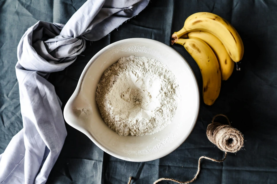 a bowl of flour next to a bunch of bananas
